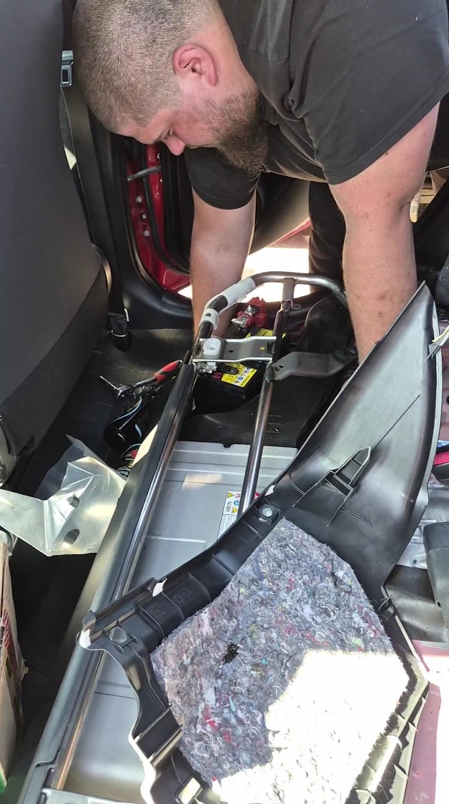 A technician working inside a car on a dismantled seat and trim assembly